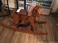 Side view of the pine wood handcrafted rocking horse showing craftsmanship, brown leather saddle, pink yarn mane, and one ear missing.