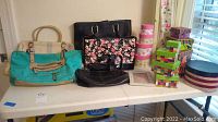 Overall view of lot items on folding table including various handbags, decorative storage boxes, and a round tissue holder box