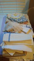 White vintage linens with blue stripes folded on a table alongside beige lace gloves and crochet pieces.