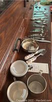Overview of Lunt sterling bowl, adult flatware, baby cups and ceramic baby utensils arranged on wood surface