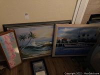 Four pieces of marine themed artwork including two large oil on canvas paintings and two framed prints propped against a wall.