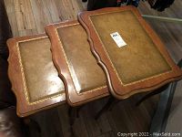 Photo of all three vintage nesting tables stacked together showing their rectangular shape, curved wooden edges, and inlaid tops with gold floral borders.
