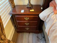 Full view of the nightstand placed next to a bed, showing its design and finish.