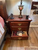Front angled view of the nightstand showing three drawers, top with items (lamp, phone holder), and brass handles.
