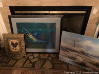 Lot of three framed artworks arranged by a fireplace including the signed oil on canvas beach scene, rooster print, and marlin print.