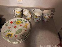 Stack of eight snack plates and eight matching tea cups showing butterfly and floral designs in multiple colors.
