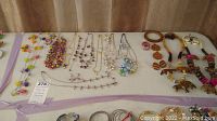 Overview of multiple necklaces laid out on surface including colorful beaded and metallic necklaces as well as wooden jewelry pieces.