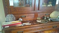 Photo showing multiple silver and silver plated items arranged on wooden furniture, including forks, trays, and serving pieces.