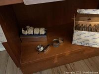 Sterling silver napkin rings positioned next to boxed lead crystal coasters on wood shelf.