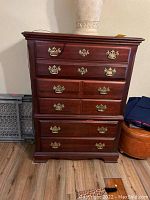 Front view of wooden tall boy dresser showing 5 drawers with brass handles and some scratches on surface.