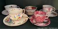 Five vintage tea cup sets with various floral and scenic designs shown together.