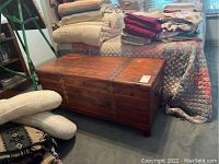 Full view of the rectangular wooden chest next to a bed and blankets, showing the top, front, and side with metal corner supports and rivets.