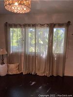 Four linen curtain panels hanging on a window with visible sunlight filtering through, showing their light brown/beige semi-sheer fabric.