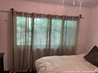 Four beige linen curtain panels hung on metal rod with decorative finials, shown in bedroom.
