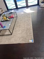 Full view of a beige-toned 8x10 area rug under a glass coffee table on dark hardwood floor.