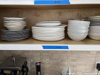 Top shelf with stacks of assorted dinnerware including plates and bowls: white dinner plates, textured speckled plates, and white bowls