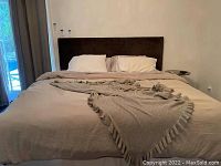 Bed with beige fitted sheet, beige flat sheet, two beige pillowcases, two white pillowcases and decorative beige ruffled blanket