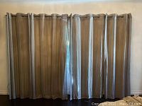 Wide view of four grey linen curtains hanging on metal rods on a window wall.