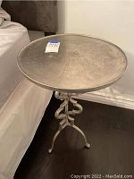 Full view of the metal round end table next to a couch, showing the round smooth top and decorative metal base.