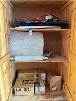 Wooden cabinet shelves with bubble wrap, plastic wraps, and cardboard boxes containing various items