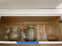 Glass pitchers and other glassware viewed inside a cabinet shelf