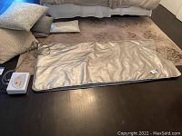 Full view of the silver infrared sauna blanket laying flat on floor with digital control unit attached.