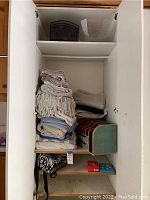 Cabinet with folded linens and small games on lower shelf, file sorter and lunch bag on middle shelf