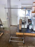 Full view of metal rolling clothing rack showing vertical poles, horizontal hanging bar and caster wheels.