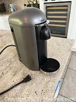 Nespresso coffee machine on kitchen counter with visible power cord and plug, drip tray, and water reservoir.