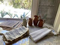 Overview of pitchers arranged on a countertop along with folded fabric runners and placemats nearby