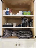 Cabinet shelves with placemats, napkins, hand blender box, votive tray, and lightbulb boxes