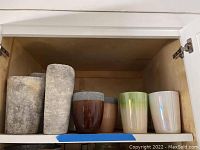 Seven pots and vases on wooden shelf showing variety in colors and textures.