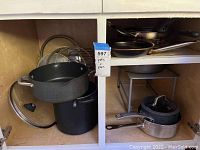 Overall view of pots and pans in shelving, shows various cookware and lids stacked and organized.