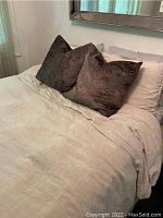Photo of queen bed made with cream colored top sheet or comforter, three brown decorative pillows, and light gray fitted sheet visible underneath.