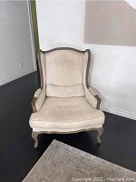 Full view of the Restoration Hardware wingback armchair against the wall showing beige upholstery, wood frame, and cushion.