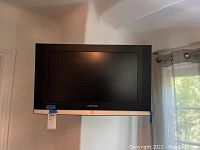 Front view of the Samsung 26-inch TV mounted on the wall with visible Samsung logo and silver trim.