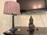 Table lamp and Buddha statue on wooden surface under TV