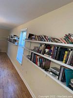 Wide shot of eight shelves filled with assorted books against a beige wall.