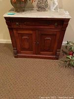 Front view of antique wooden cabinet with marble top, drawer and doors visible, items on top.