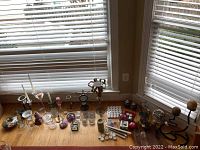 Wide view of the candle holders on a windowsill showing a variety of metal, glass, and ceramic types with some tapered candles included.