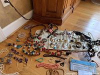 Photo showing assorted costume jewelry items laid out on the floor including necklaces, bracelets, and earrings with some pearl necklaces and colorful beads