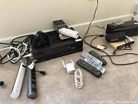 Sony VHS audio video control center with various remotes, cables, Wi-Fi extender, and power strips laid out on floor near wall.