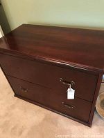 Front view of wooden file cabinet showing two drawers and one missing pull on the top drawer.