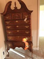Front view of the wooden highboy dresser showing brass pulls, spiral finial, decorative shell carving, and cabriole legs.
