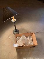 Metal base lamp standing on the floor next to an open box filled with several new lamp shades still in packaging.