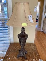 Full view of composite base table lamp with beige fabric shade showing its detailed design and finial damage.