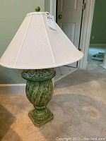 Full view of the lamp showing the white fabric lampshade and the green ceramic urn-style base with fruit details on top.
