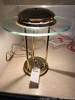 Full view of metal and glass lamp showing transparent round glass top, metal rods and weighted base with electrical cord.