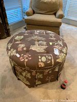Round upholstered ottoman with brown fabric featuring palm tree and botanical pattern. Button tufted top surface, pleated skirt base. Visible stains present.