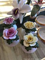 Close-up of floral salt and pepper shakers with pink, yellow, and lavender flower tops and green leaf bases alongside partial view of porcelain salt cellars.